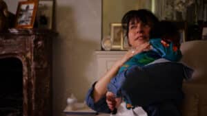 A woman in a cozy room holds a child enjoying safe sleep, nestled in a colorful hoodie. The brown marble fireplace, framed photos, and cabinet with decorative items enhance the warm and peaceful atmosphere against subtly patterned walls. Night Nannies London